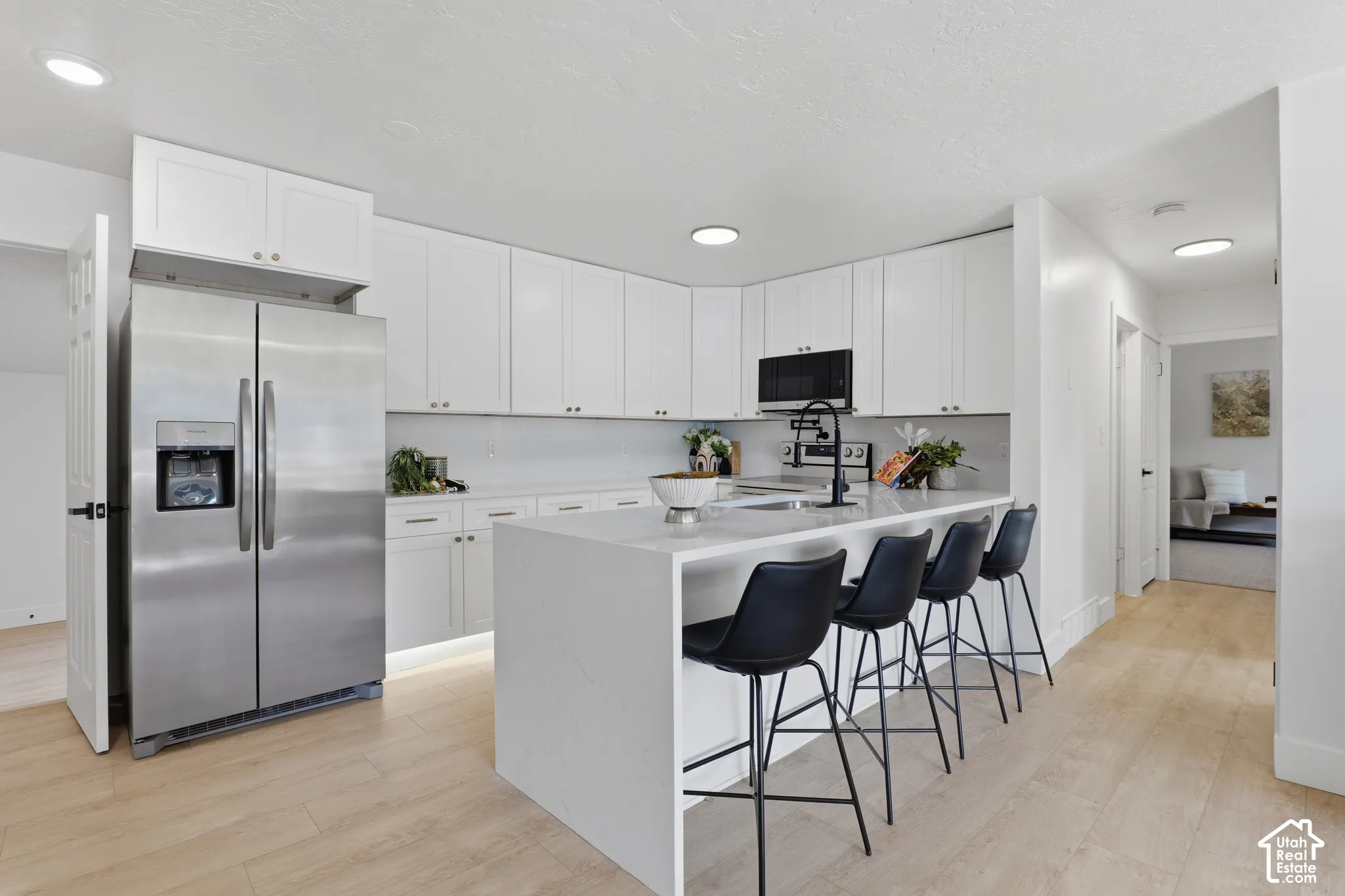 Kitchen featuring white cabinetry, solid-surface countertops, wood-finish flooring, stainless steel side-by-side refrigerator, and a matte black faucet