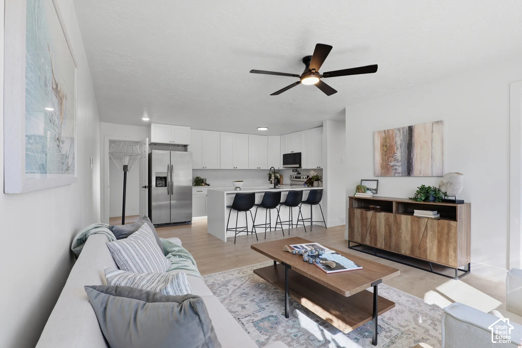 Kitchen featuring white cabinetry, stainless steel appliances, and a central island with countertop seating, complemented by wood-finish flooring and a matte black ceiling fan