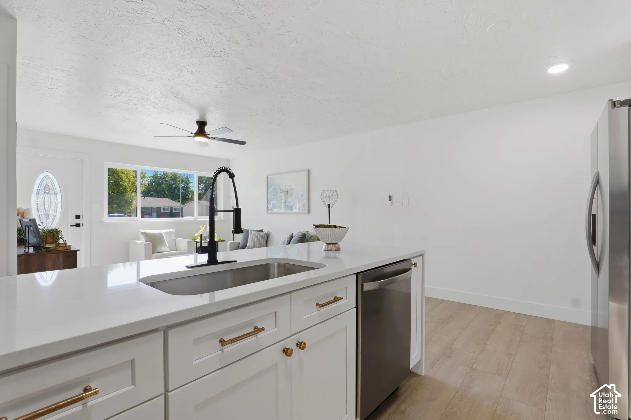 Kitchen island featuring a solid-surface countertop, an undermount rectangular sink, a matte black high-arc pull-down faucet, white shaker-style cabinetry with brass-tone hardware, and wood-finish flooring