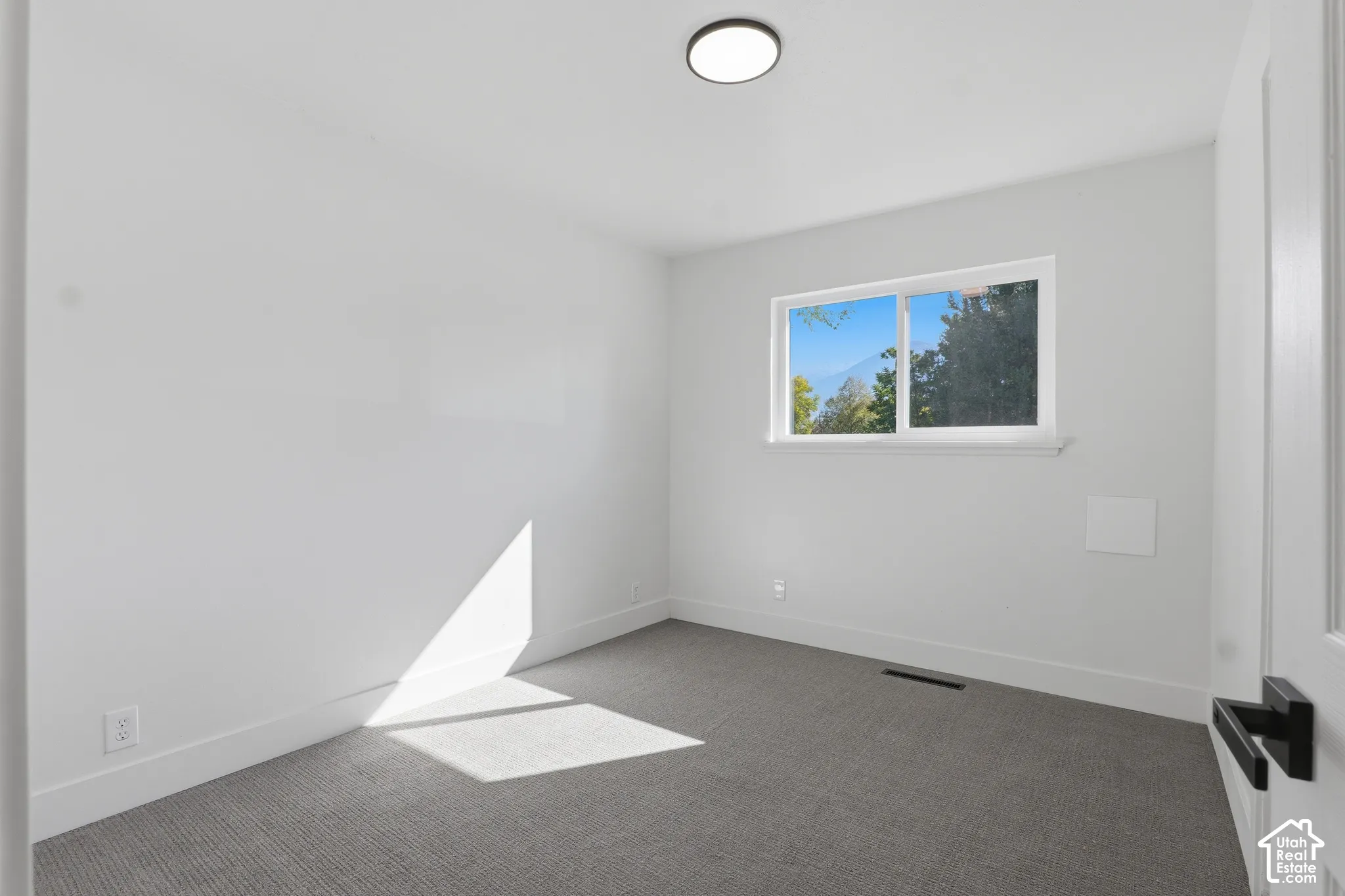 Neutral-toned interior space featuring wall-to-wall carpeting, a sliding window with mountain scenery, and a minimalist flush-mount ceiling light fixture