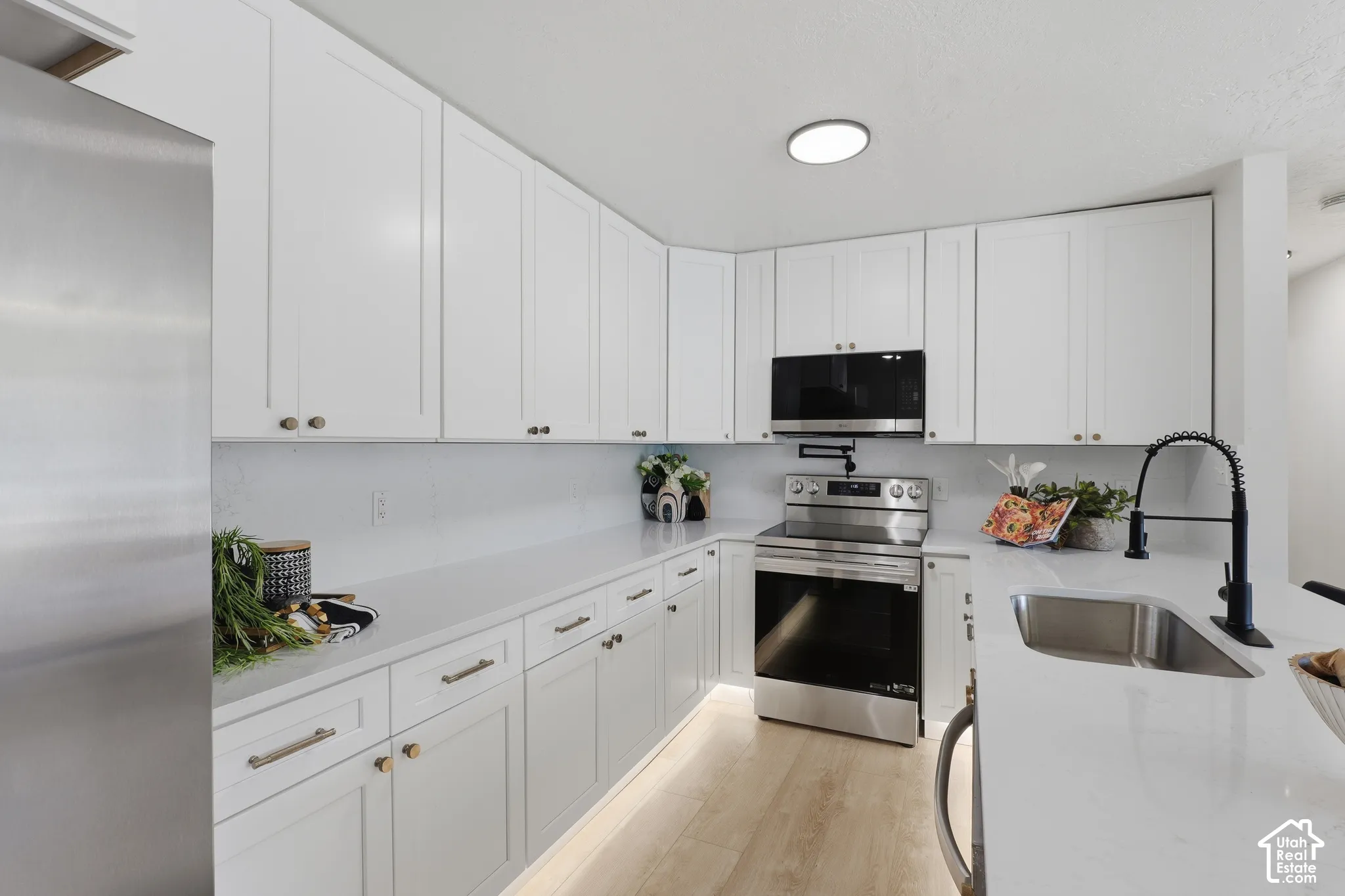 White shaker-style cabinetry, quartz countertops, stainless steel appliances, matte black gooseneck faucet, and wood-finish flooring