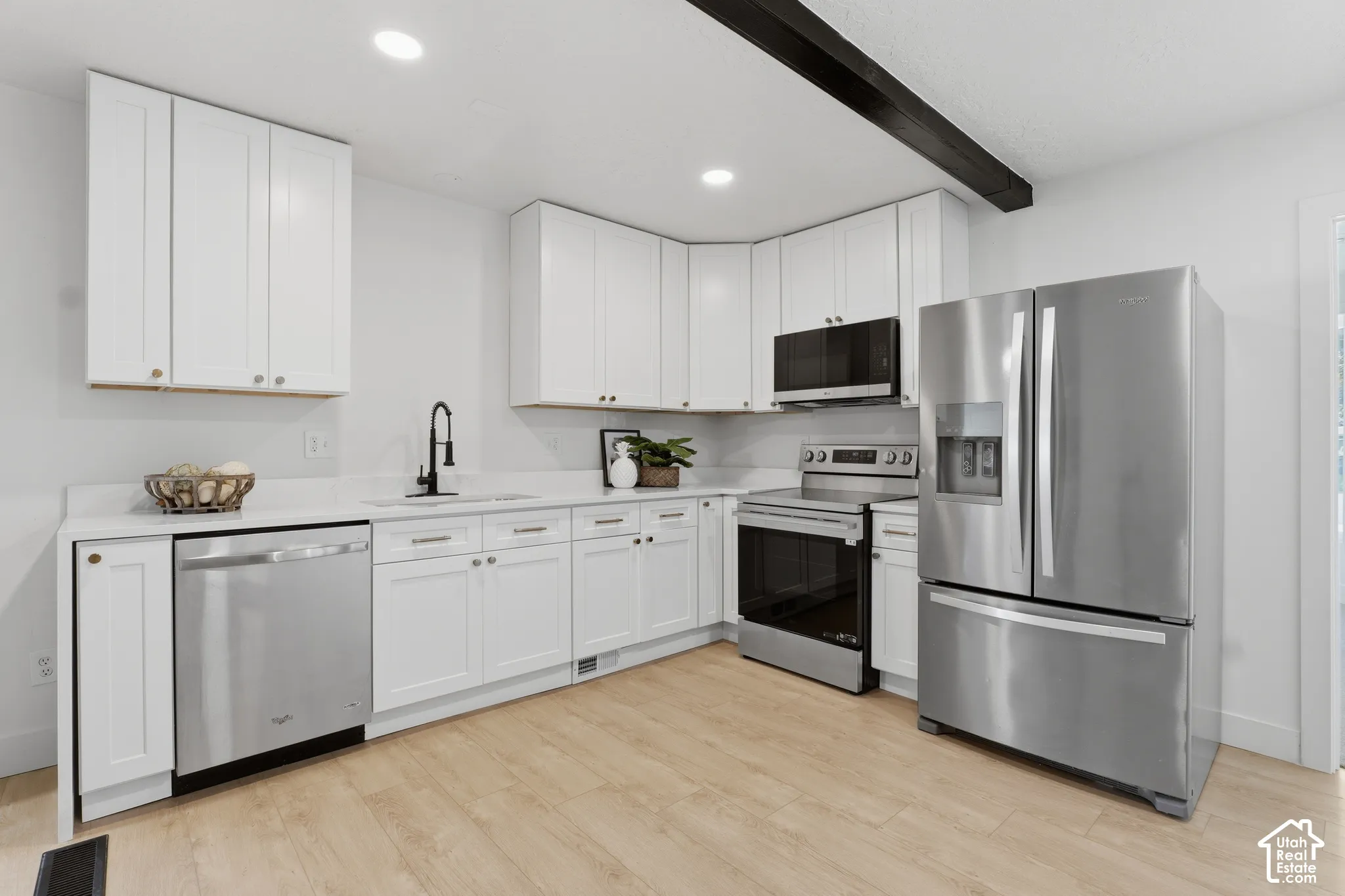 Kitchen featuring white shaker-style cabinetry, solid-surface countertops, stainless steel appliances, a matte black faucet, and wood-finish flooring