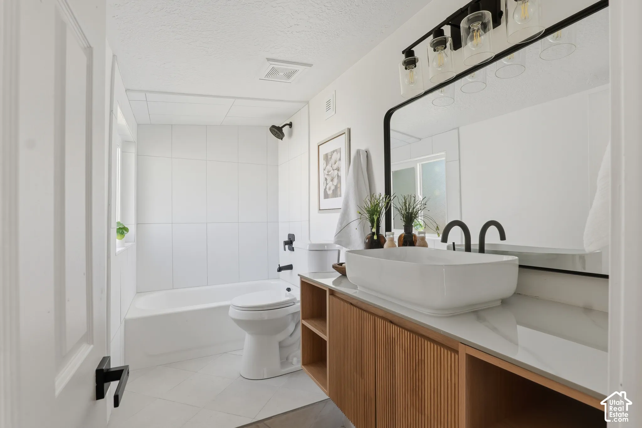Custom vanity with a reeded wood-finish cabinet and integrated shelving, stone-finish countertop with a rectangular vessel sink, matte black hardware, and floor-to-ceiling tile surround in the tub area