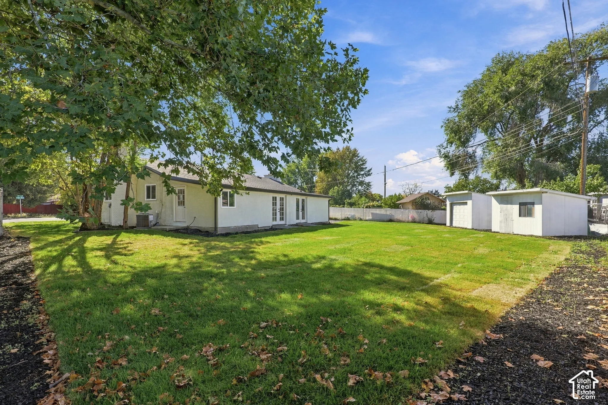 Expansive backyard featuring a large grass lawn, mature trees, mulched borders, and an exterior storage structure