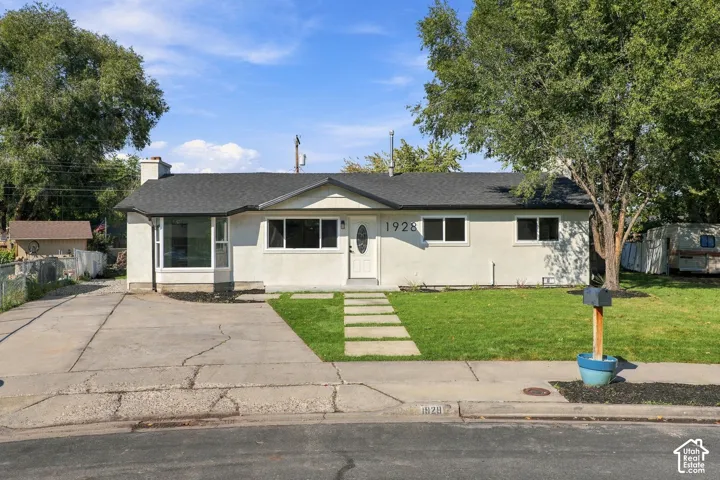 Single-story exterior featuring light-toned stucco siding, a composition shingle roof, a front bay window, and a concrete paver walkway