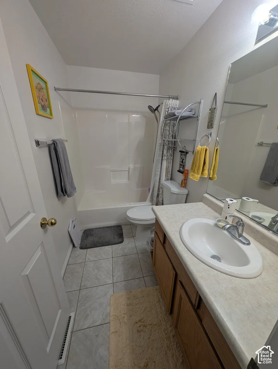 Bathroom featuring a vanity with neutral-toned laminate countertop, integrated sink, chrome faucet, wood-finish cabinetry, and ceramic tile flooring