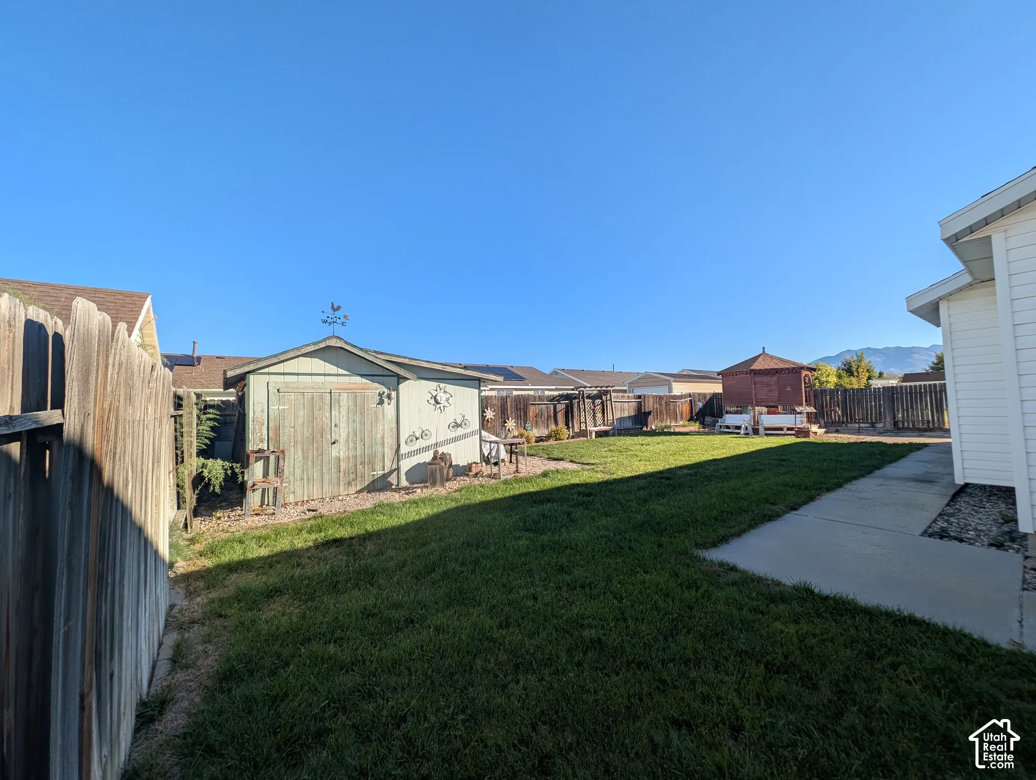 Fenced backyard featuring a manicured lawn, concrete patio, storage shed, and detached gazebo