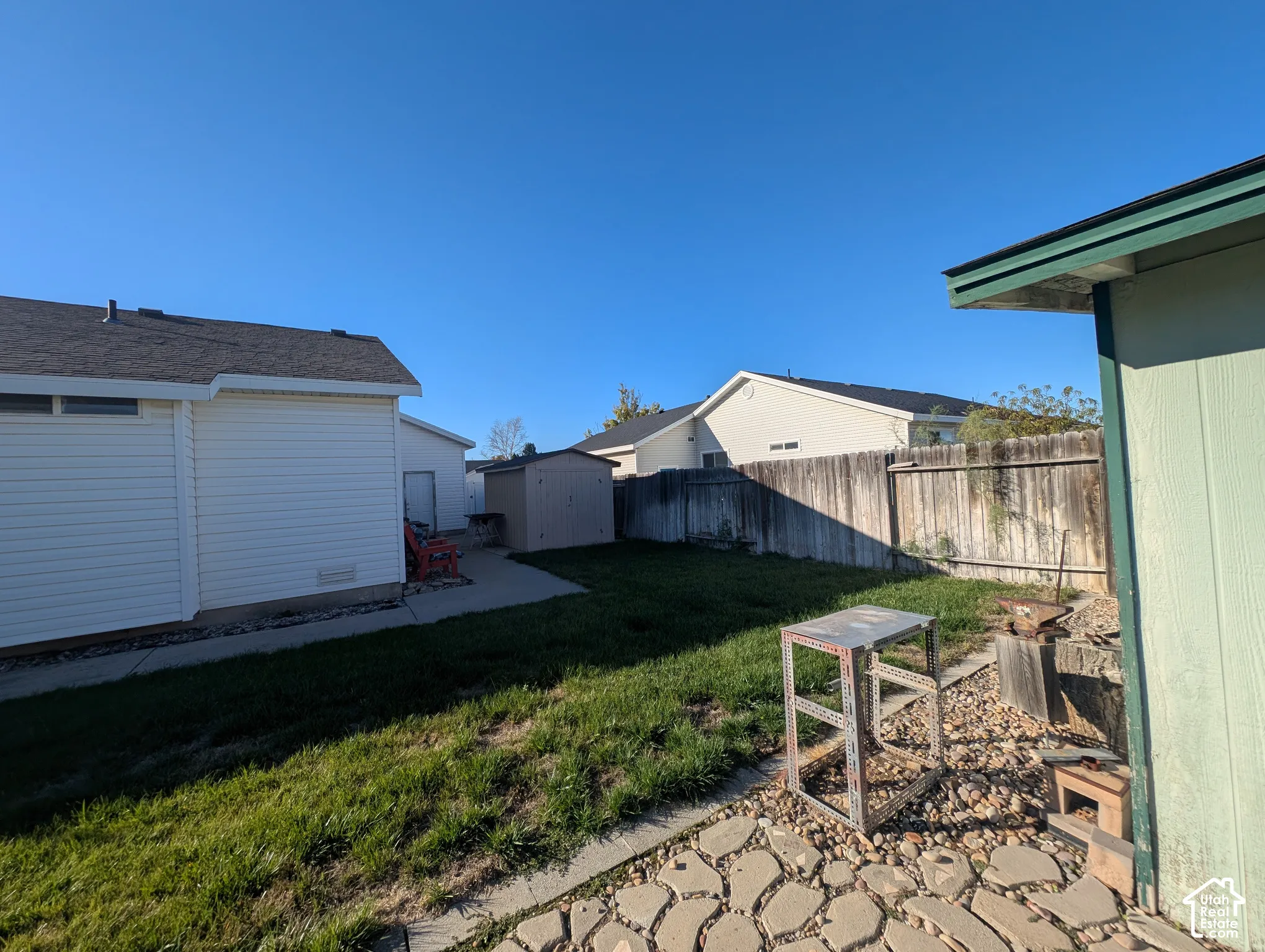 Rear yard space featuring a concrete patio, stone hardscaping, perimeter wood fencing, and an exterior storage shed