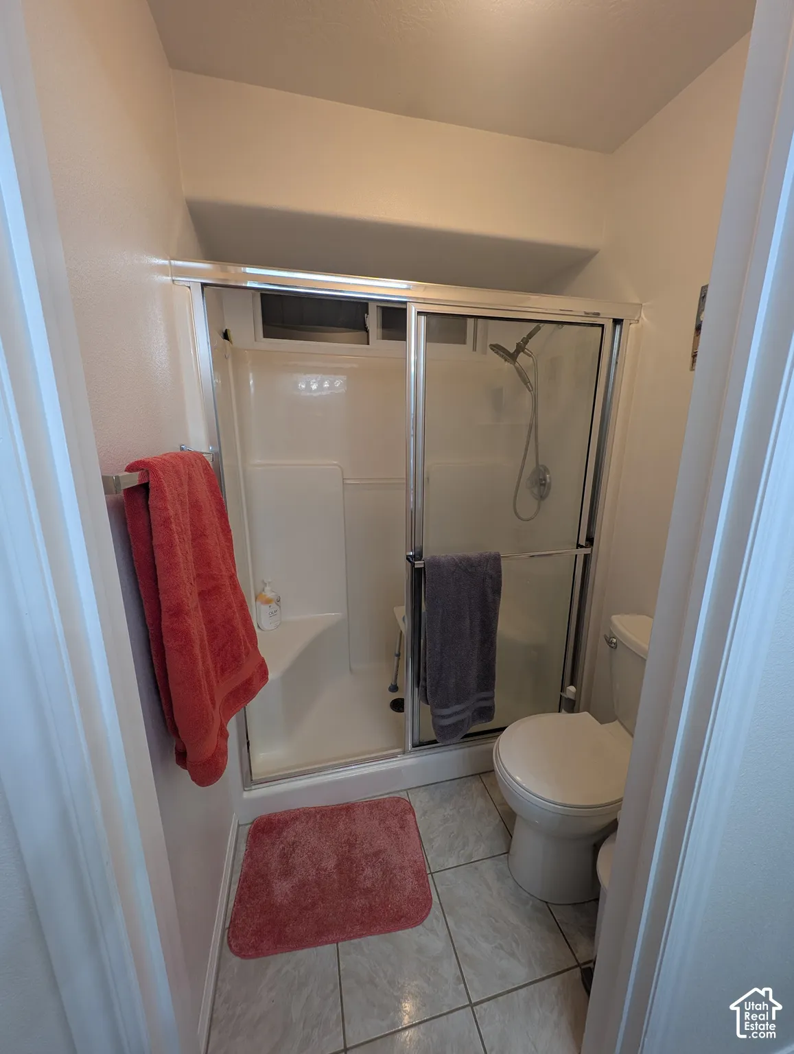 Shower stall featuring a glass-panel sliding door, built-in corner seat, and handheld shower fixture, complemented by tile flooring