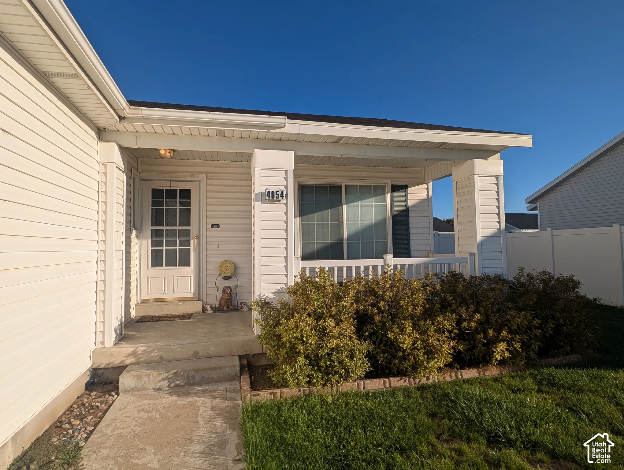 Covered front porch featuring white vinyl siding, a paneled entry door with window lights, decorative railing, and concrete steps