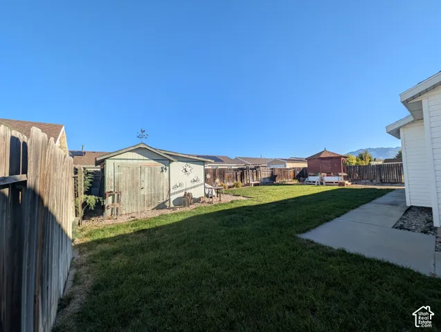 Fenced backyard featuring a manicured lawn, concrete patio, storage shed, and detached gazebo