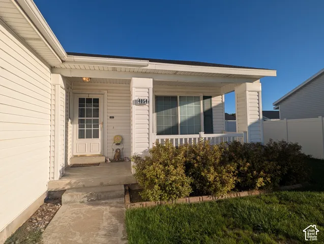 Covered front porch featuring white vinyl siding, a paneled entry door with window lights, decorative railing, and concrete steps