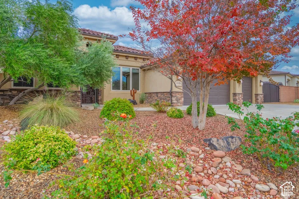 Stucco exterior featuring multi-toned stone veneer accents, concrete tile roof, attached two-car garage, and xeriscaped front yard with mature ornamental trees