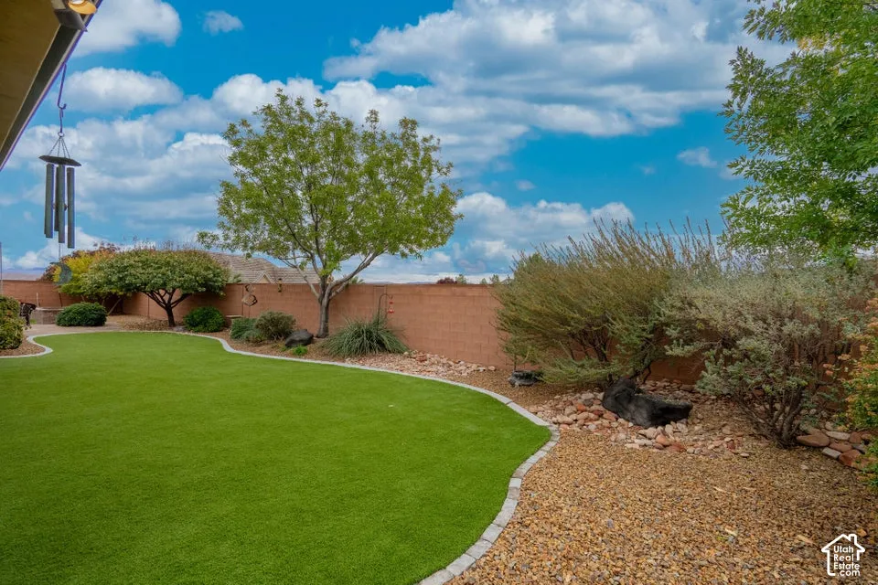 Backyard featuring artificial turf, concrete block perimeter wall, stone mulch landscaping, mature trees, and concrete paver edging