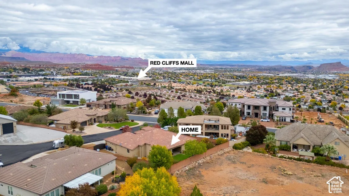 Aerial perspective of a single-story residence with a multi-hipped tile roof and a covered rear patio featuring a manicured lawn, set against a backdrop of desert landscape and mountain ranges