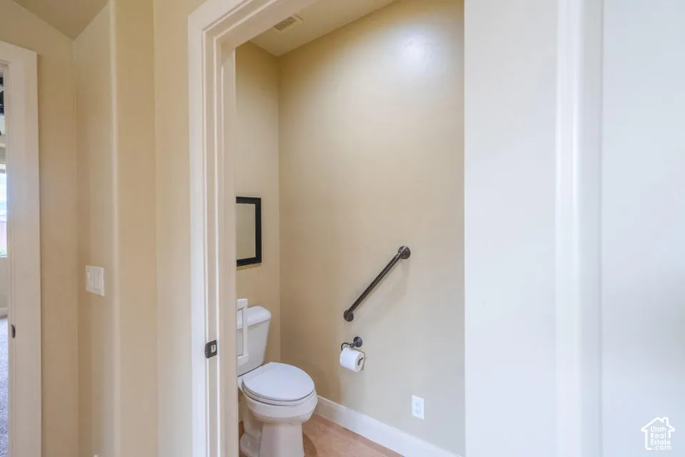 Restroom featuring a two-piece white porcelain toilet, installed dark-finish metal grab bar, wall-mounted toilet paper dispenser, and neutral wall tones