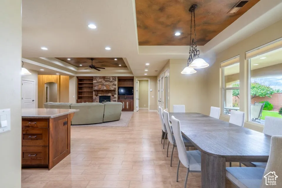 Open-concept living space featuring wood-finish tile flooring, recessed lighting, decorative tray ceilings, a natural stone fireplace with built-in cabinetry, and multi-light pendant fixtures