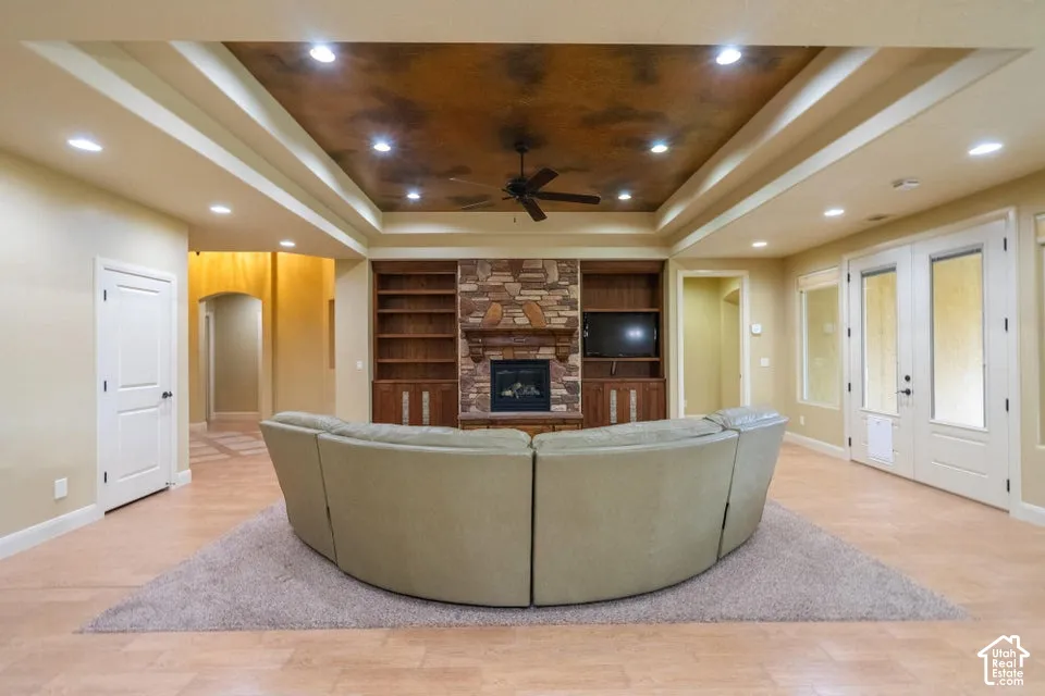 Tray ceiling with decorative finish, stone fireplace surround, built-in wooden cabinetry, recessed lighting, and wood-finish flooring