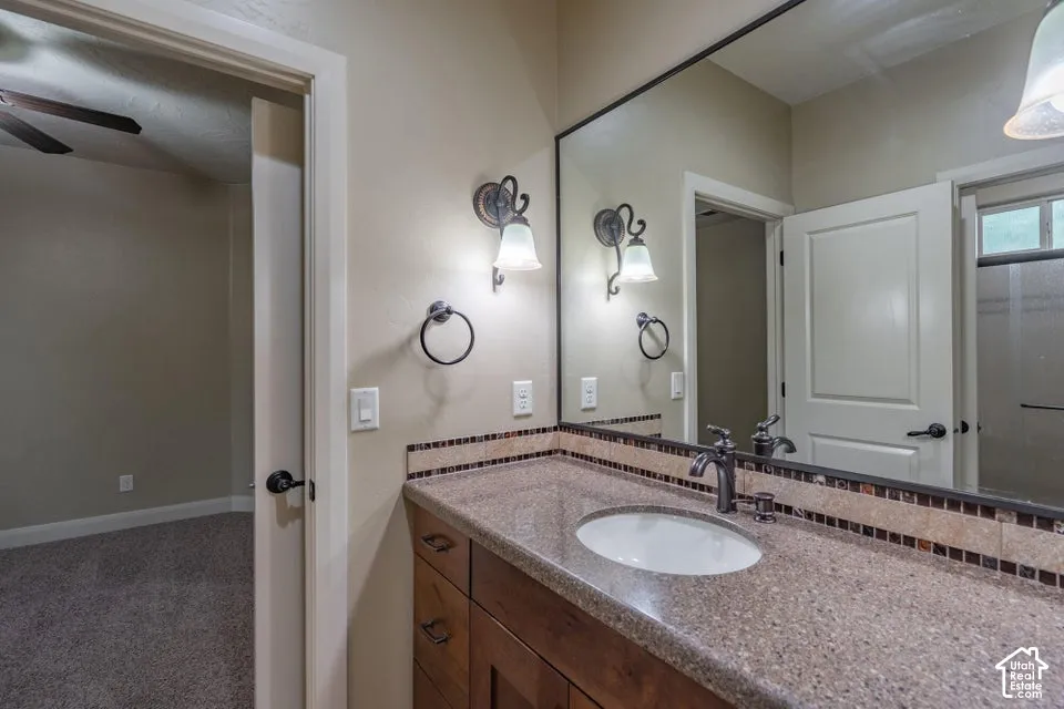 Bathroom vanity featuring a stone-composite countertop with an integrated basin, stained wood cabinetry, a large wall-mounted mirror, and decorative tile backsplash