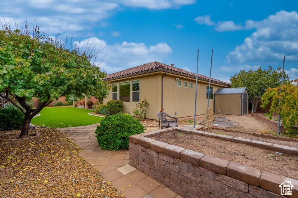 Backyard featuring a paver patio, raised block garden bed, synthetic turf lawn, and detached metal storage shed