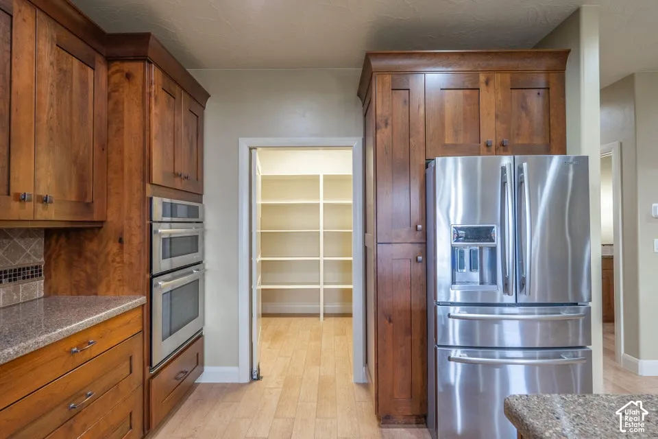 Custom wood cabinetry with crown molding, stainless steel double wall ovens, built-in stainless steel refrigerator, stone-finish countertops, and dedicated pantry space with shelving