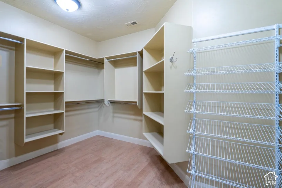 Walk-in storage space featuring wood-finish flooring, built-in laminate shelving, integrated hanging rods, and adjustable wire shelving units