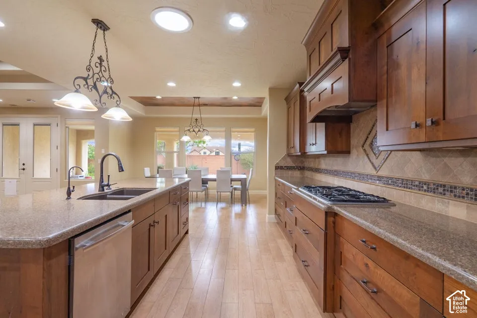 Kitchen featuring wood cabinetry, solid surface countertops, a stainless steel cooktop, tile backsplash with decorative stone inlay, and wood-finish flooring