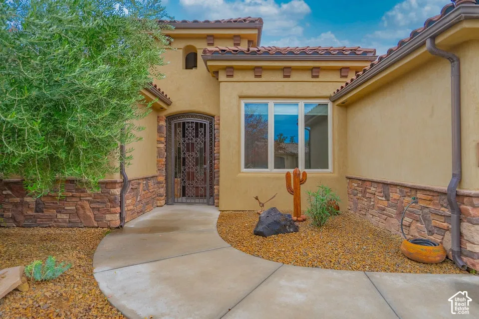 Stucco exterior featuring stacked stone veneer, tiled roofline, metal security door, and concrete walkway