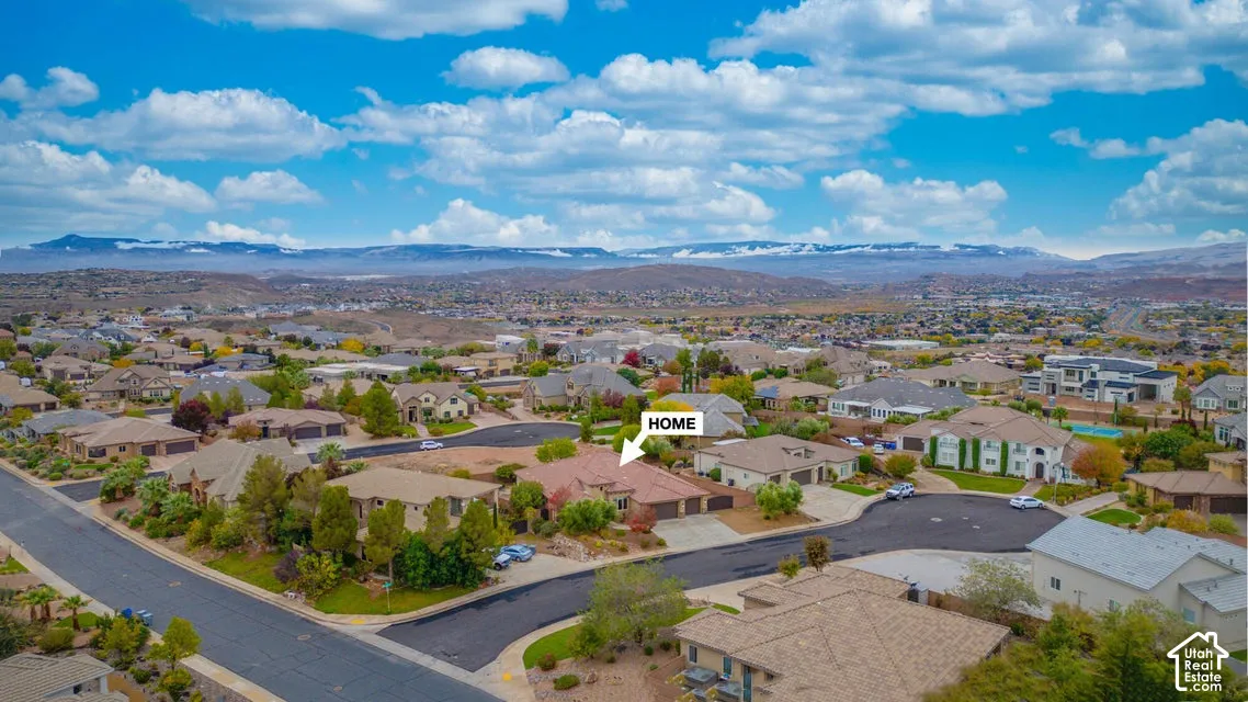 Aerial perspective of a single-level residence featuring a clay tile roof, three-car garage, concrete driveway, and a mountain backdrop