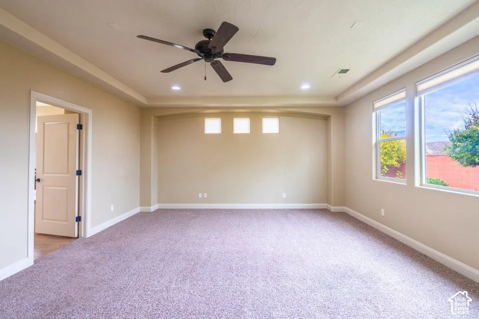 Tray ceiling with inset lighting, recessed wall alcove featuring triple clerestory windows, ceiling fan, and large windows
