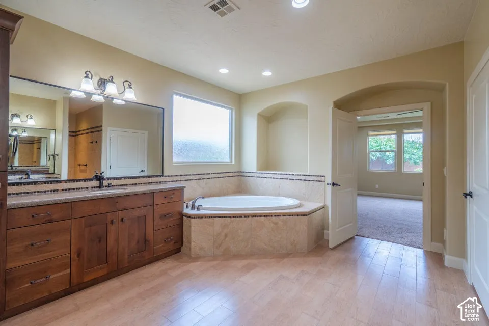 Bathroom featuring wood-finish cabinetry, stone-tile tub surround with mosaic accent, built-in recessed shelving, large wall mirror, and tile flooring