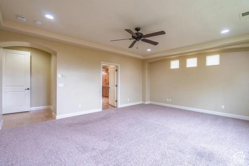 Spacious room featuring a tray ceiling, recessed lighting, a dark-finish ceiling fan, neutral carpeting, and three transom windows