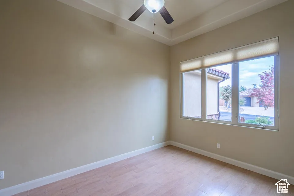 Room featuring a tray ceiling, wood-finish flooring, and a ceiling fan with integrated lighting