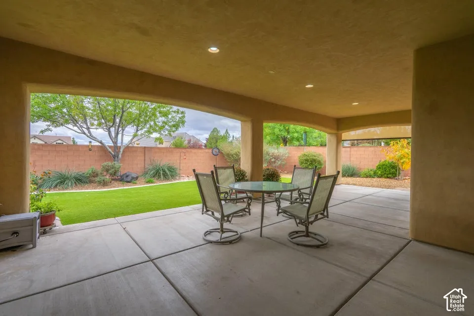 Covered concrete patio featuring recessed lighting, expansive stucco pillars, a level lawn, and a masonry perimeter wall