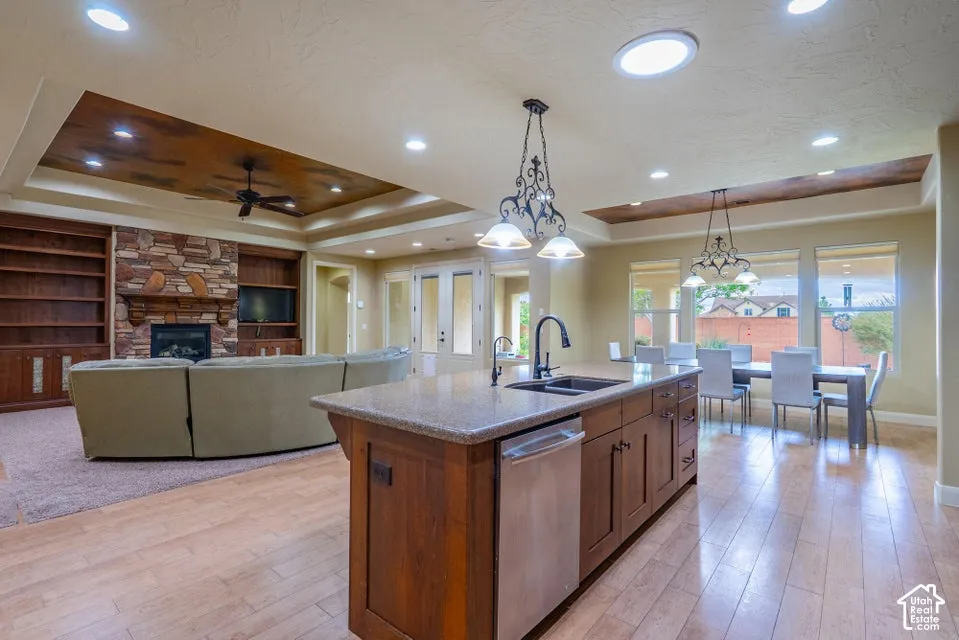 Kitchen island with stone countertop, wood-finish cabinetry, built-in stainless steel dishwasher, and under-mount sink