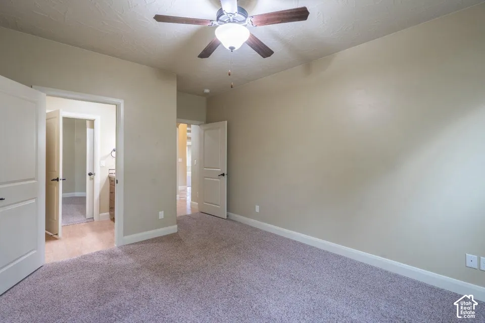 Neutral-toned interior featuring wall-to-wall carpeting, multi-panel interior doors, and a ceiling-mounted light fixture with an integrated fan