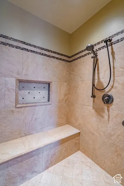 Walk-in shower featuring natural stone wall tile, an integrated stone bench, a recessed wall niche, a multi-function handheld shower head, and a decorative mosaic tile border