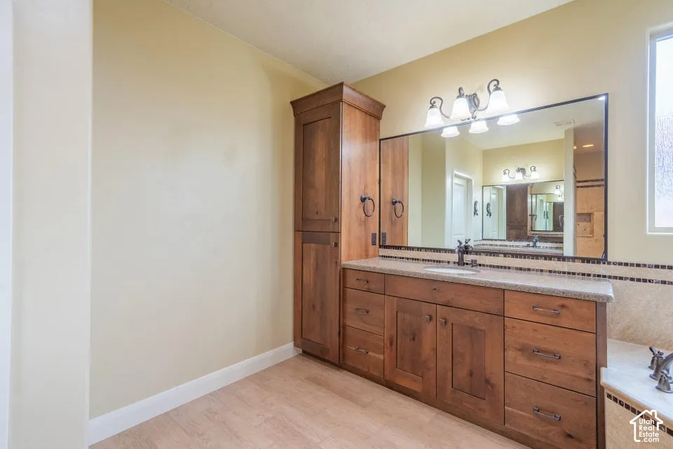 Vanity featuring stained wood cabinetry, tall integrated storage tower, stone-style countertop, large rectangular mirror, and four-light overhead fixture