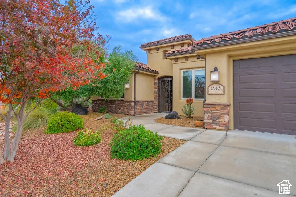 Stucco exterior featuring stacked stone accents, tile roof, concrete driveway, and ornamental metal entry gate