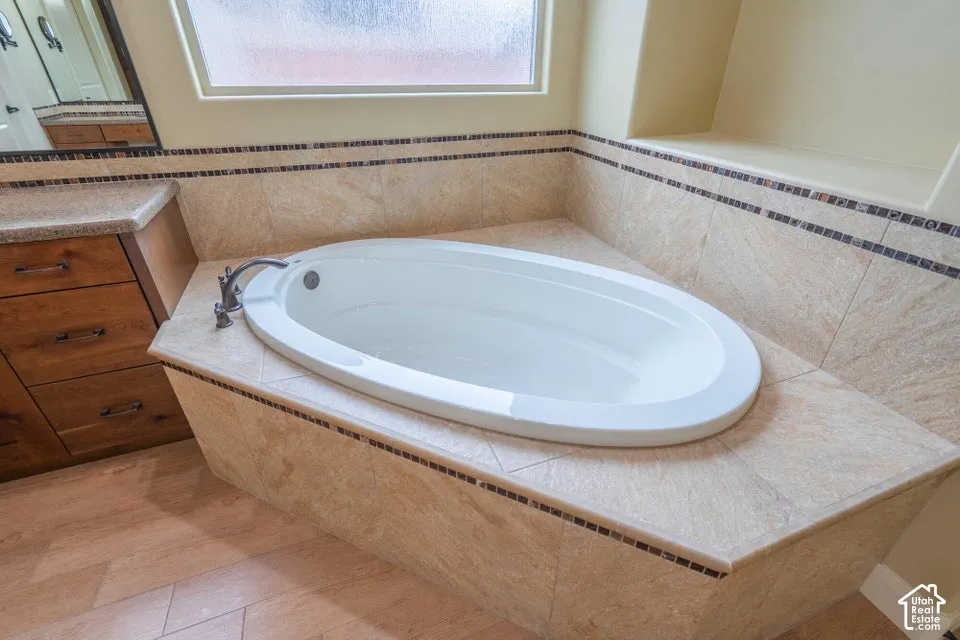 Oval soaking tub set within a tiled deck featuring decorative mosaic accents, wood-finish vanity cabinetry, and a recessed wall niche