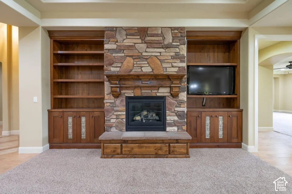 Floor-to-ceiling stone fireplace featuring a wood mantel, built-in shelving, custom cabinetry with decorative inlays, and a raised hearth