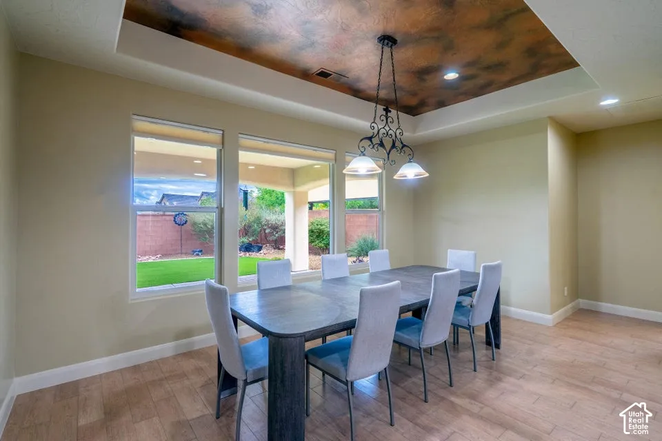 Tray ceiling with decorative finish, ornate iron chandelier, wood-finish flooring, and large windows looking out to a covered patio