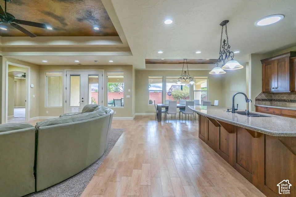 Open-concept area featuring wood-finish flooring, tray ceilings with recessed lighting, a kitchen island with stone countertop, and custom wood cabinetry