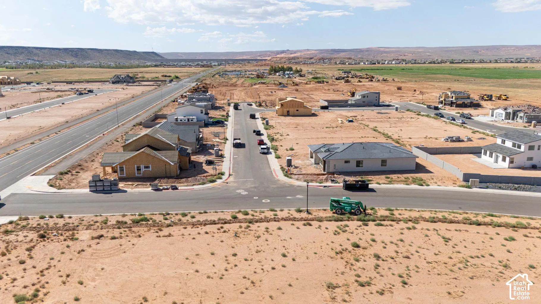 Aerial perspective of a developing residential subdivision featuring paved asphalt roads, concrete curbing, and expansive desert landscape with mountain silhouettes