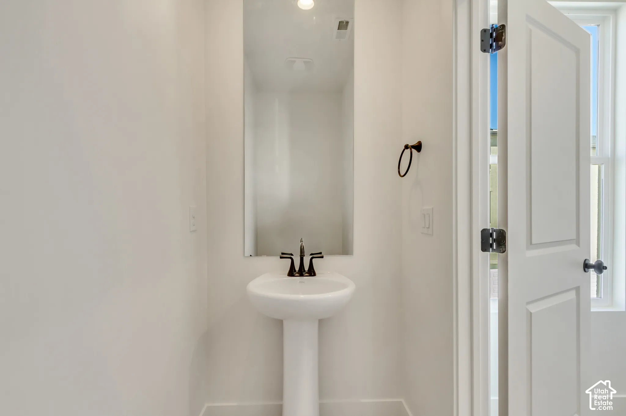 Pedestal sink with dark metal faucet, full-height wall mirror, and dark metal towel ring
