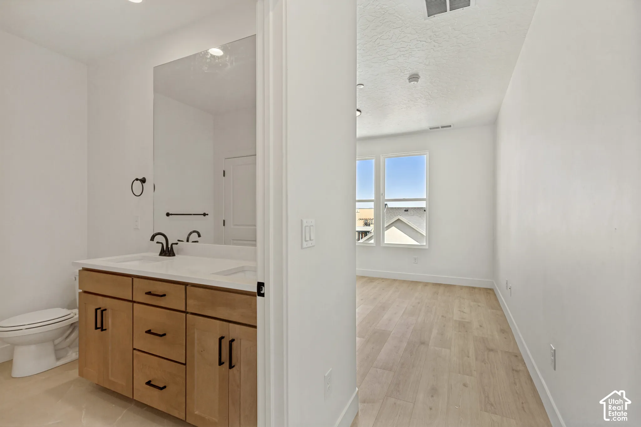 Bathroom featuring light wood-finish cabinetry, a white countertop with an integrated sink, matte black hardware, and wood-finish flooring extending into the room