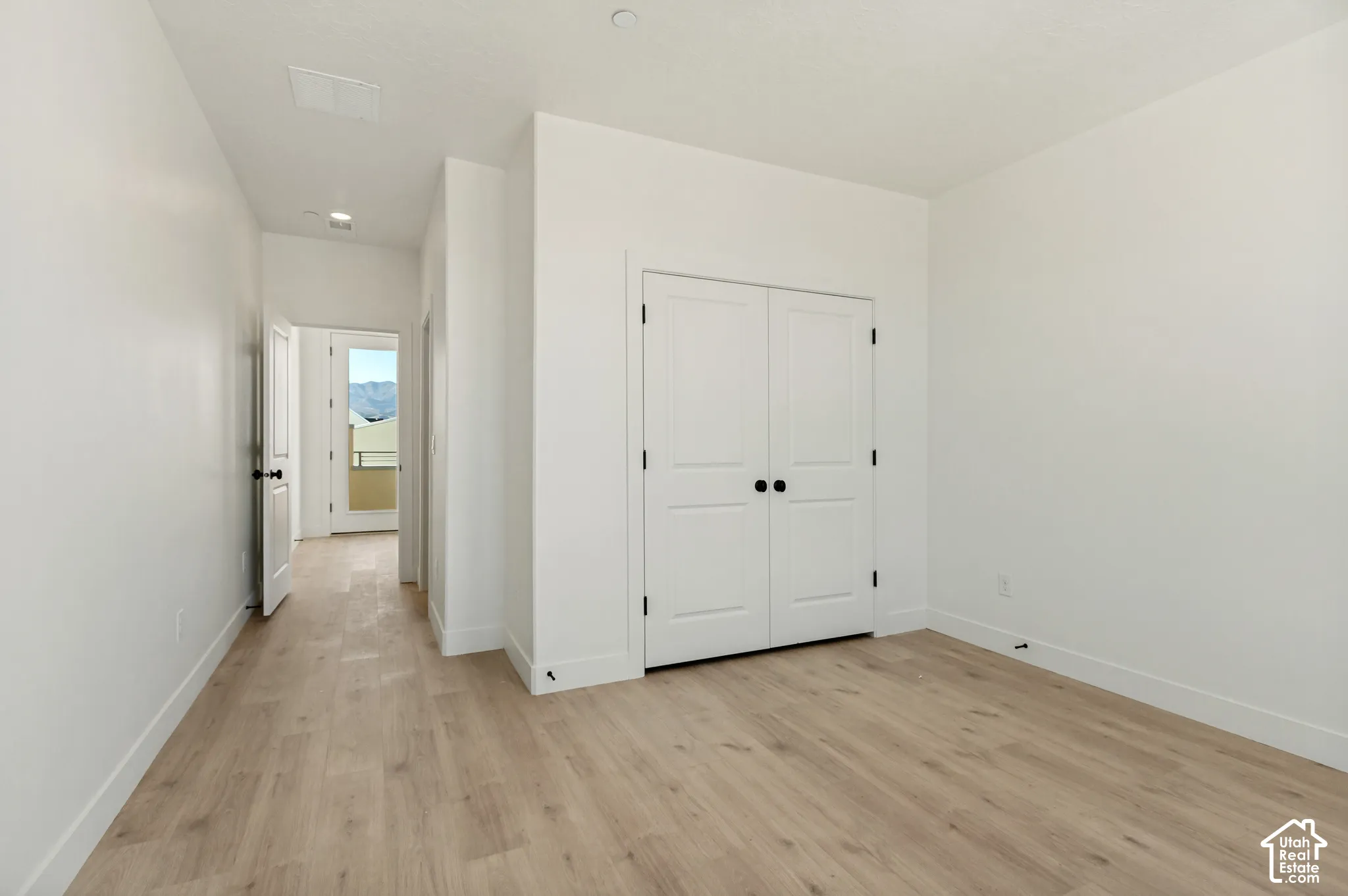 Interior room featuring wood-finish flooring, double-panel closet doors with matte black hardware, and crisp white wall finishes