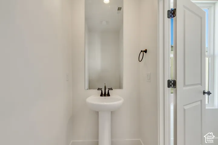 Pedestal sink with dark metal faucet, full-height wall mirror, and dark metal towel ring
