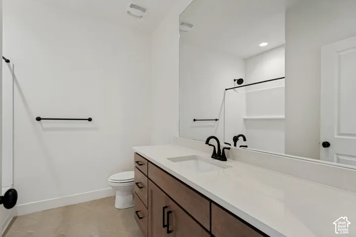 Bathroom featuring a vanity with wood-finish cabinetry, light-toned stone-style countertop, undermount sink, matte black hardware, and an expansive wall-mounted mirror