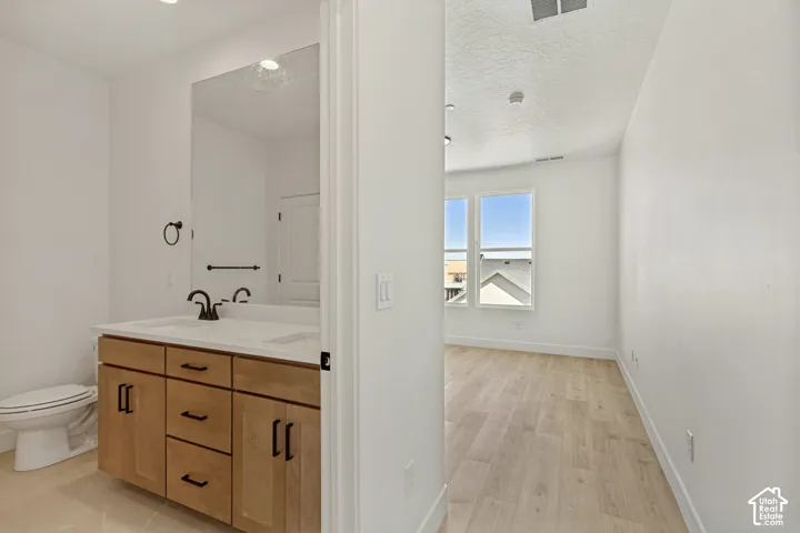 Bathroom featuring light wood-finish cabinetry, a white countertop with an integrated sink, matte black hardware, and wood-finish flooring extending into the room